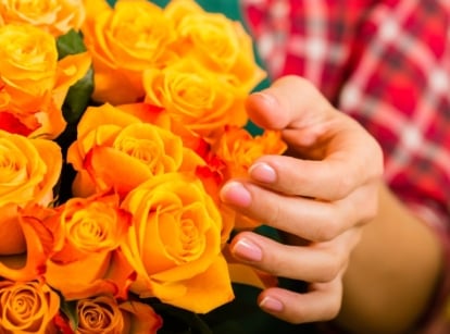 A close-up shot of a person in the process of inspecting and tending to a composition of orange colored flowers, showcasing florist roses tips