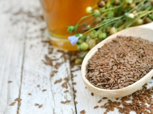 A close-up shot of a wooden spoon filled with seeds, alongside plants, showcasing when to harvest flaxseed