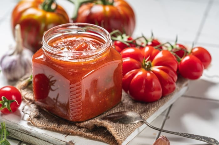 A shot of a jar of homemade sauce made from fresh red fruits, showcasing tomato varieties for making salsa