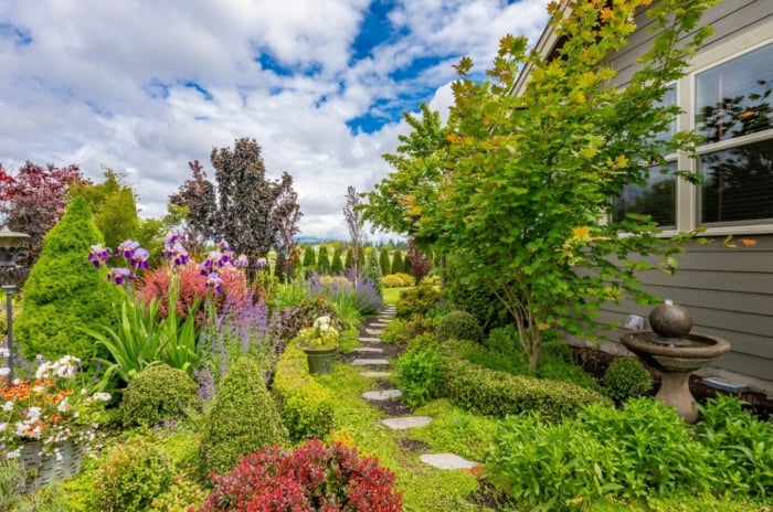 A beautiful garden with a mix of colorful flowers, trees, and trimmed bushes, with an added pathway through the scenery.