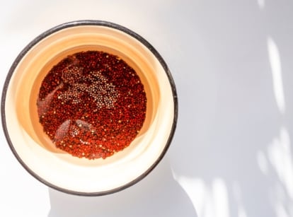 A round bowl with seeds soaking in reddish-brown water, creating a contrast of dark seeds against the lighter edges of the liquid, with a soft light illuminating the surface.