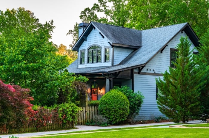 A light blue house surrounded by diverse year-round foundation plants including a red-leafed shrub, a spherical green shrub, and a conical evergreen.